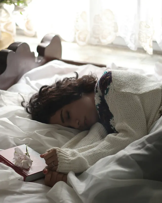 Mulher de suéter dormindo tranquila em uma cama de lençóis brancos